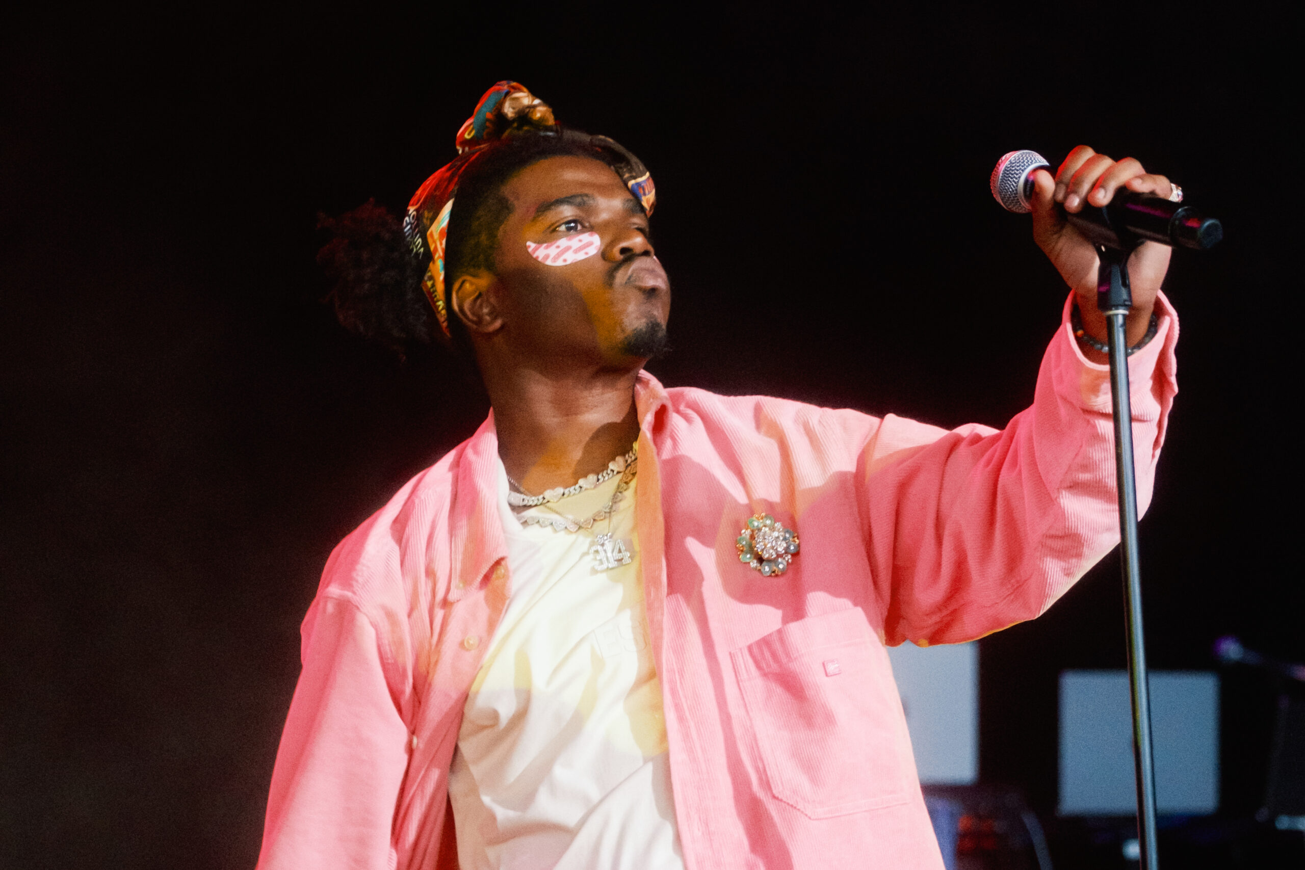 Rapper Smino performing on stage, wearing a pink shirt and a apatterned headscarf.
